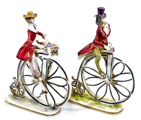 A pair of Capodimonte style penny farthing figures, each polychrome decorated predominantly in pink, black and yellow, unmarked, 31cm high.