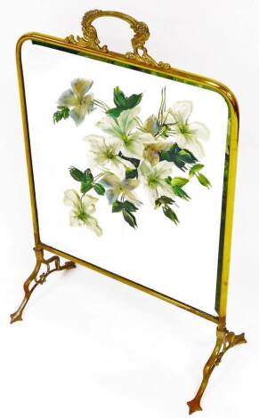 An early 20thC brass framed fire screen, with painted glazed centre set with flowers on shaped legs with inverted heart shaped central motif, 75cm high, 47cm wide, 28cm deep.