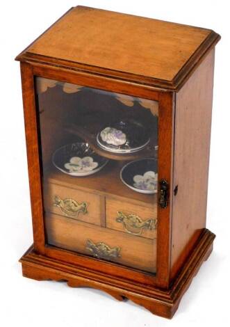 An Edwardian oak smoker's cabinet, of rectangular form, with plain glazed door and fitted interior, with two short and one long drawers, on stylised bracket feet, complete with various mixing items, etc., 43cm high.