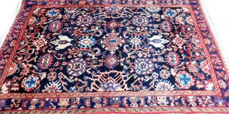 A Persian rug, with a design of medallions and other devices on a deep navy ground with one wide and two narrow borders, 141cm x 247cm.