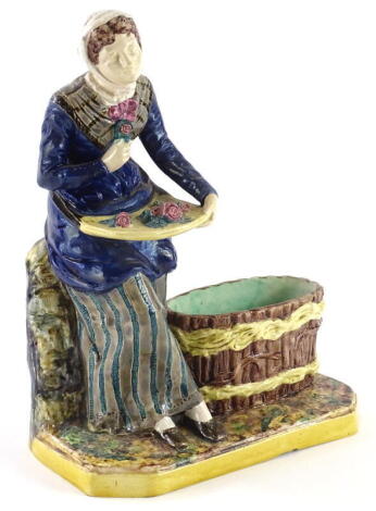 A late 19thC continental majolica match holder, modelled in the form of a lady seated with a basket full of flowers, beside an empty basket on a canted rectangular base, impressed marks to underside T.S., 24.5cm high.