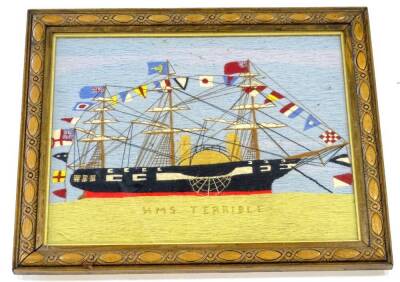 A late 19thC wool work picture of HMS Terrible, the Battleship adorned with various flags, in carved oak frame, 49cm x 59cm overall.