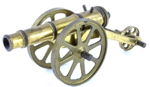 A miniature brass cannon, on a three wheel brass carriage with spoked wheels.