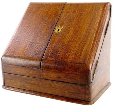 An Edwardian oak slope top stationery cabinet, the hinged lid enclosing a fitted interior with an inkwell, 30cm wide.