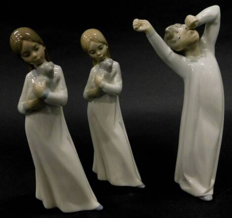 A Lladro porcelain figure of a young boy wearing a night dress yawning, and two similar Nao figures each with a puppy. (3)