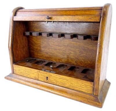 An Edwardian oak pipe rack, with a domed tambour door, enclosing fitted interior, with recess on a plinth base, 26cm high, 35cm wide.