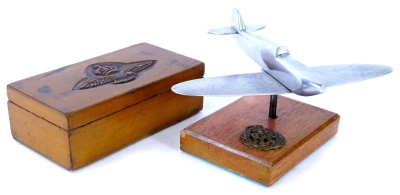 An aluminium desk ornament, modelled in the form of an aeroplane, on a rectangular mahogany base, applied with RAF badge, and a military cigarette box, carved with eagle and crown emblem.