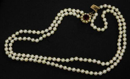 A two row cultured pearl necklace, one row with 70 pearls 5.5mm x 4.7mm, the other with 73 pearls 5.5mm x 4.9mm, with a circular yellow metal clasp, set with a 9mm garnet, surrounded by ten 3.5mm cultured pearls, all set with claw setting, stamped 9ct, wi