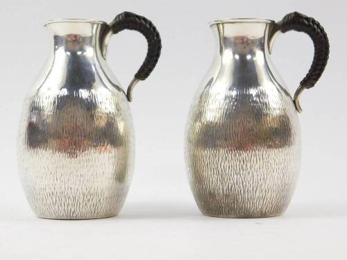 A pair of Japanese silver jugs, with leather bound handles, of bulbous form, with textured decoration, bears four character mark, 11.5cm high, 6.06oz.