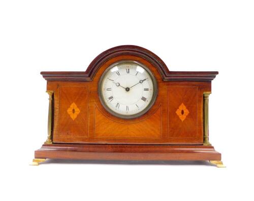 An Edwardian mahogany and inlaid mantel clock, circular dial bearing Roman numerals, clockwork movement with integral key, the case of architectural form, with brass columns, raised on brass bracket feet, 20cm high, 31cm wide, 9.5cm deep.