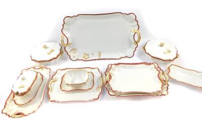 A Havilland Limoges porcelain part dinner service, moulded and gilt heightened with a floral sprig, within a red repeating flower head border, comprising six graduated twin handled platters, a pair of vegetable tureens and covers, a pair of sauce tureens