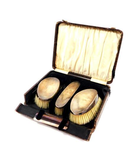 A George V silver backed four piece dressing table set, with engine turned decoration, square reserve, cased, comprising a pair of hair brushes, clothes brush and a comb, Birmingham 1933.