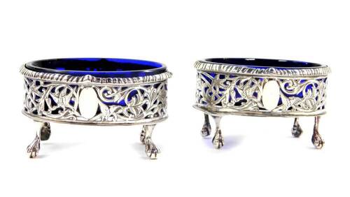 A pair of Victorian silver oval salts, with blue glass liners, pierced and engraved with birds and scrolling leaves, raised on four ball and claw feet, Thomas Hayes, Birmingham 1900., 3.94oz.