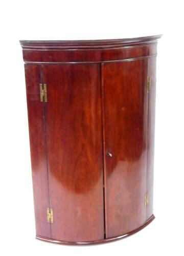 A George III flame mahogany bow front hanging corner cupboard, with satin lined interior shelves, 114cm high.