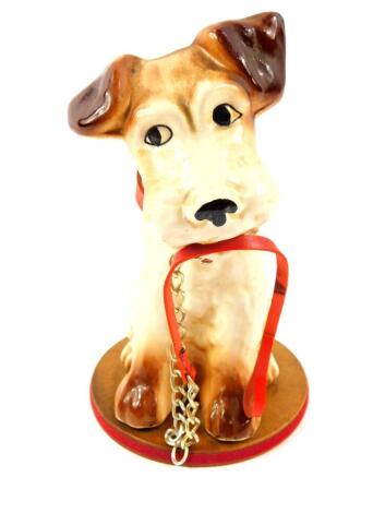 A mid 20thC pottery figure of a seated terrier, with a collar and lead, raised on a brown plastic figure base, 19cm high.