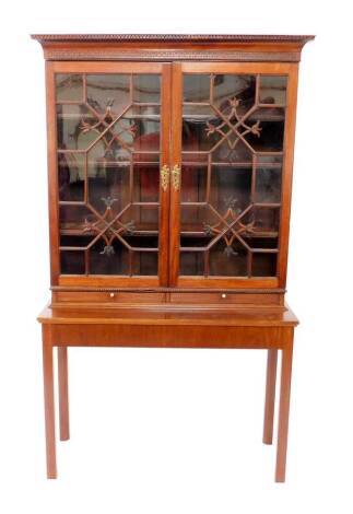 A Chippendale style mahogany bookcase on stand, the outswept pediment with dentil moulding and blind fretwork, over two astragal glazed doors, with foliate detailing, opening to reveal three shelves, edged with cock beading, over two frieze drawers, on a 