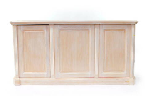 A limed oak sideboard, with three doors opening to reveal drawers and shelves, raised on a plinth base, 178cm wide, 53.5cm deep, 90cm high.