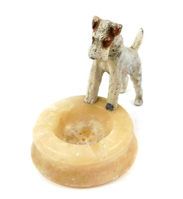 An early 20thC alabaster ashtray, surmounted with a cold painted lead figure of an Airedale terrier, 20cm wide.