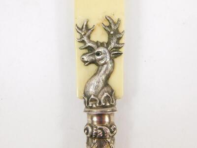 A Scottish late 19thC ivory paper knife, with a horn handle, and white metal mount, cast as the heraldic crest of a deer, set with coloured glass eyes, 35cm wide.