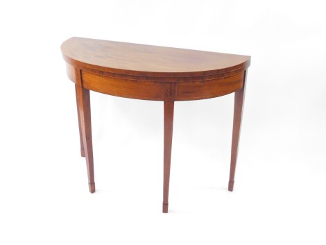 A George III mahogany demi lune card table, with satin wood cross banded folding top with baize insert, cross banded frieze with oval inlays over the square taper legs, 96cm diameter.