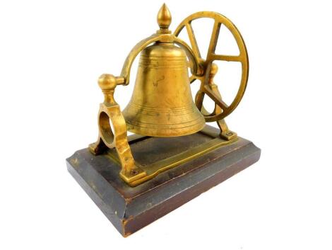 A brass bell form table bell, raised on a wooden base, 18cm wide, 12cm deep.