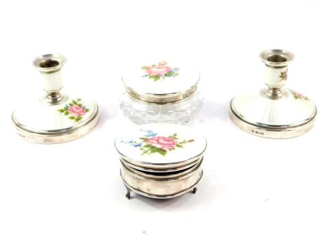 A cut glass silver and guilloche enamel four piece dressing table set, painted with roses against a white ground, comprising powder box and cover, circular jewellery box raised on three feet, and a pair of loaded candlesticks, Birmingham 1963 - 64.