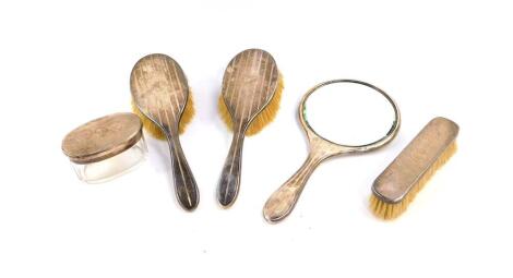 A George V silver backed dressing table set, with engine turned decoration, circular reserve engraved 'Kathleen', comprising a pair of hair brushes, and a hand mirror, Birmingham 1915, together with a George V cut glass toilet jar with silver lid, and a