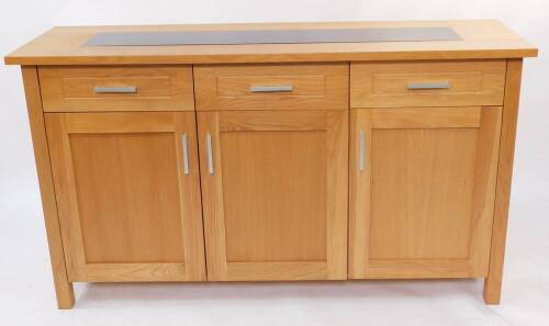 A light oak sideboard, the top inset with black glass, over three drawers above cupboard doors, raised on square block feet, 85cm high, 150cm width, 46cm deep.