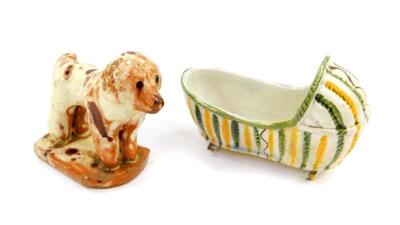 A Staffordshire early 19thC pearl ware cradle, 10cm wide, together with a slip ware figure of a dog, modelled standing on a oval base, 10cm wide. (A/F) (2)