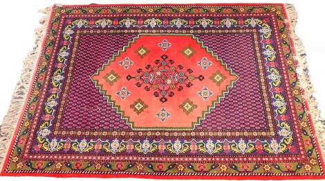 A Caucasian red ground rug, the central field decorated with floral motifs, within a border of botehs and repeating flowers and leaves, 275cm x 172cm.