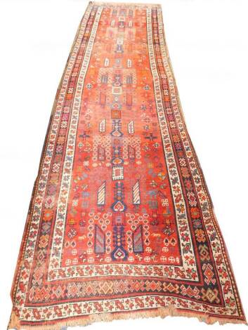 A Caucasian red ground runner, decorated with a geometric and floral repeating motifs, within floral borders, 412cm x 114cm.