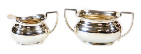 A George V silver two handled sugar bowl, 10cm high and milk jug each with angular handles of cape form on oval feet, Birmingham 1929, 17oz.