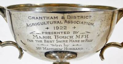 A George V silver trophy, of circular form with ear handles, on a turned stem and circular foot, marked Grantham and District Agricultural Association 1922 won by Mr Matthew Hubbard of Eaton, Birmingham 1921, 12cm high, on an ebonised plinth base, 6.8oz o - 2