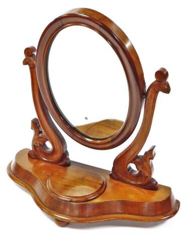 A Victorian mahogany table mirror, the oval glass flanked by floral scroll supports on a shaped base with circular lid on compressed bun feet, 54cm high.