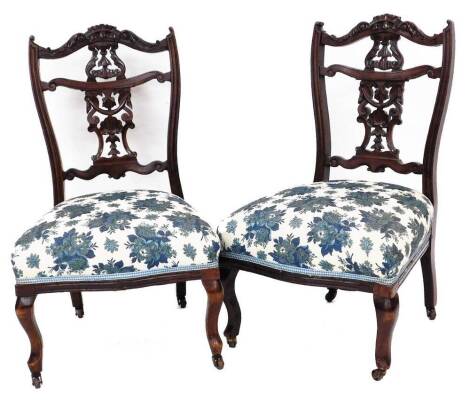 A pair Victorian children's salon chairs, with elaborate cresting rails, pierced shell and scroll back splats, overstuffed seats in later floral material on shaped front legs terminating in castors, 77cm high.