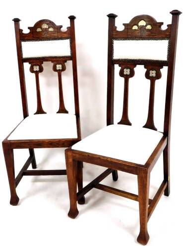 A pair of late 19thC Art Nouveau oak chairs, with arched top rails, compressed square finials and overstuffed backs and seats in (later) studded white material, each raised and inlaid with lotus flowers on square tapering front legs, joined by a H stretch