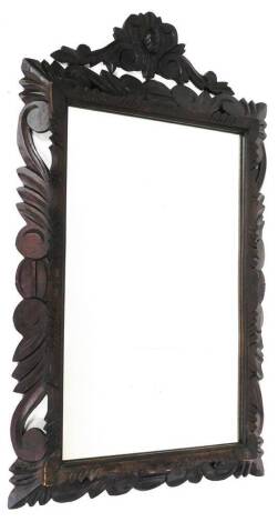 A very early 20thC carved oak mirror, the plain glass in a heavily carved frame, with scrolls, flower heads and leaves, 115cm high, 80cm wide, 12cm deep.