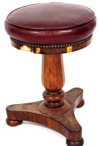 A Victorian rosewood framed piano stool, with a circular top in red leather, partially studded, on a turned stem and tricorn base terminating in compressed bun feet, 51cm high, the seat 36cm diameter.