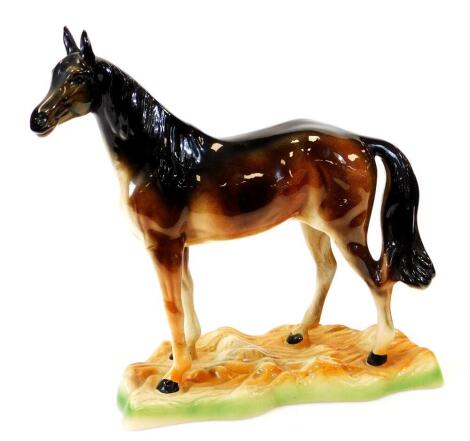 A late 20thC pottery model of a bay horse, standing on a naturalistic base, unmarked, 39cm high.