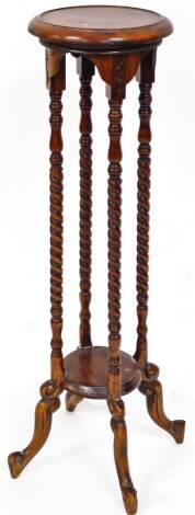 An early 20thC mahogany plant stand, the circular top on quadruple baluster and turned stems, joined by an under tier beneath, on shaped scroll feet, 100cm high, 27cm diameter.