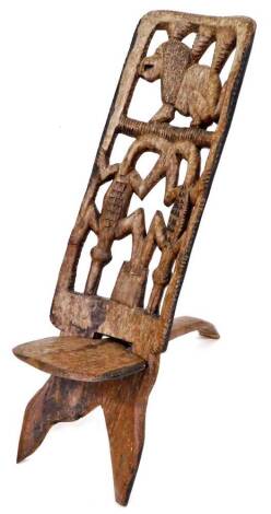 A heavily carved African tribal chair, profusely decorated with a pierced crocodile and lion back splat, on a low shaped seat, terminating in shaped stiles, 95cm high.