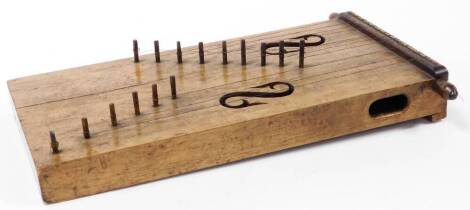A 19thC stringed tribal style zither type instrument, of square block form with lyre carving and crude pegs, set with ten strings, 44cm wide.