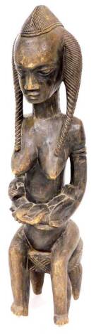 A 19thC heavily carved African tribal figure of a seated lady, with flowing hair on a stool, 98cm high.