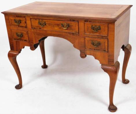 A George III style walnut lowboy, the rectangular crossbanded top quarter veneered with one long and four short frieze drawers, with swan neck handles and pierced back plates on cabriole legs, terminating in pad feet, 77cm high, 104cm wide, 52cm deep.