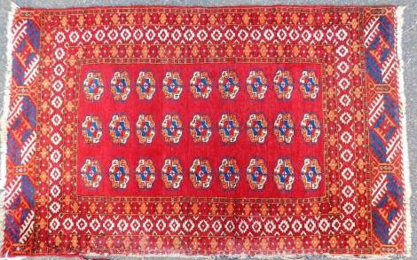 A 20thC Mauri style Turkoman design rug, of rectangular form with an outer field decorated with flowers on a red ground, the inner section with a repeat set of three banks of further floral rosettes, 130cm x 80cm.