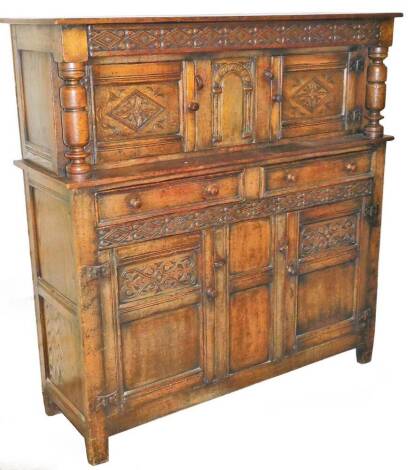 A Jacobean style oak court cupboard, of rectangular form, the upper section with a carved cornice on cylindrical supports, above a single cupboard flanked by further cupboards, with two drawers and double cupboards beneath, on block stiles, 138cm high, 13