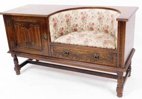 An Old Charm style oak finish linen fold telephone seat, with overstuffed embroidered seat, panelled cupboard and single drawer on turned legs, terminating in block and compressed bun feet, joined by a H stretcher, 73cm high, 123cm wide, 48cm deep. The u