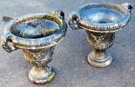 A pair of stone classical urns, each of campana form, with leafy acanthus capped scroll handles, with part gadrooned bodies, on inverted stems and circular dentil feet, 54cm high, 64cm wide, 49cm deep. (2)