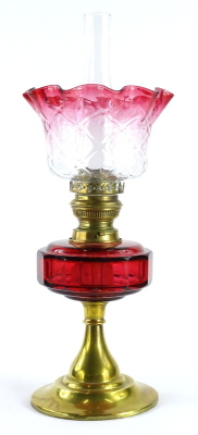 A late 19th/early 20thC oil lamp, with a part cranberry tinted shade, a ruby tinted reservoir and a tapering brass base, 50cm high overall.