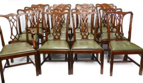 A set of sixteen mahogany dining chairs in George III style, each with a pierced splat and a green leather padded seat, on channelled legs with H stretcher, one with arms.